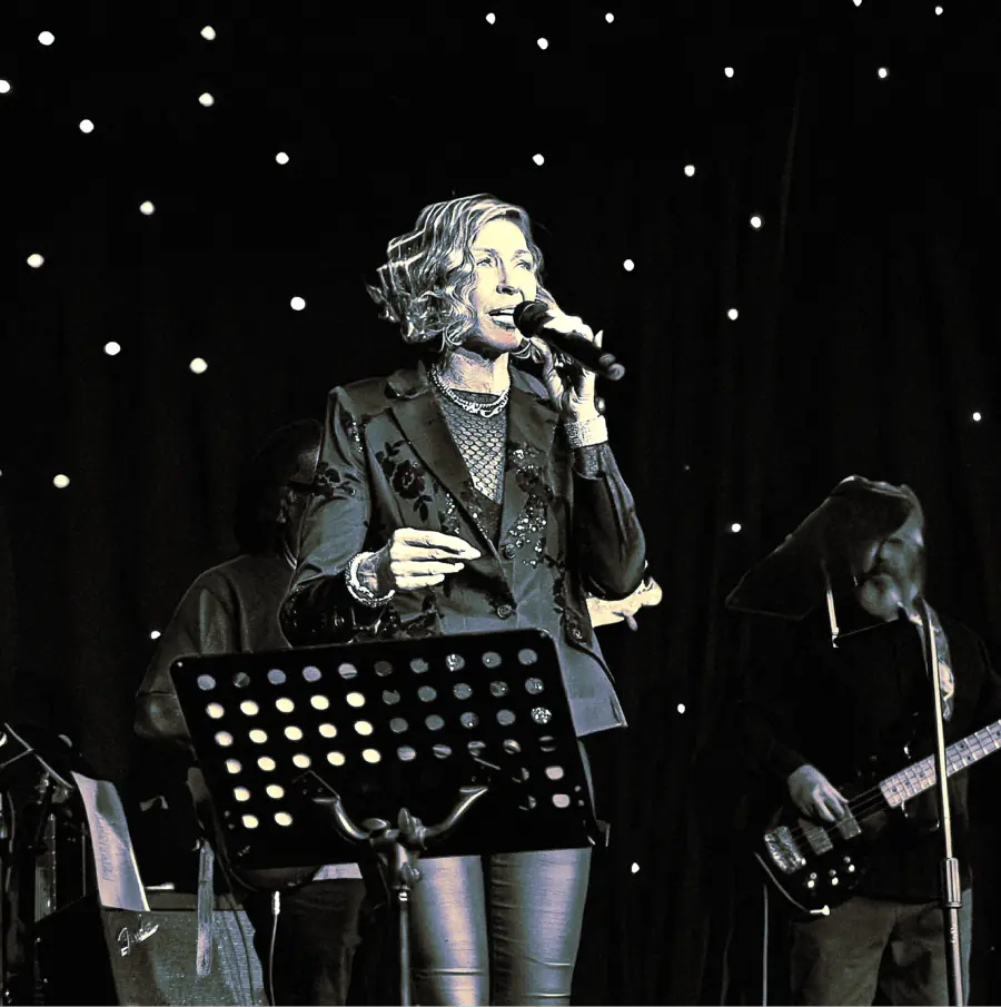 Black and white photo of Denise Choate singing on stage with musicians behind her