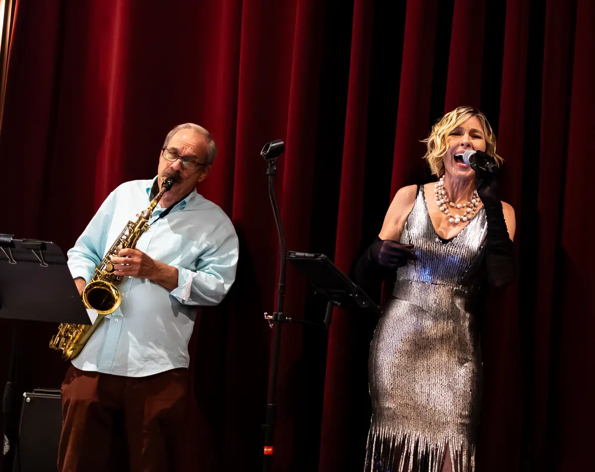 Denise Choate singing beside saxophonist Paul Contos on stage